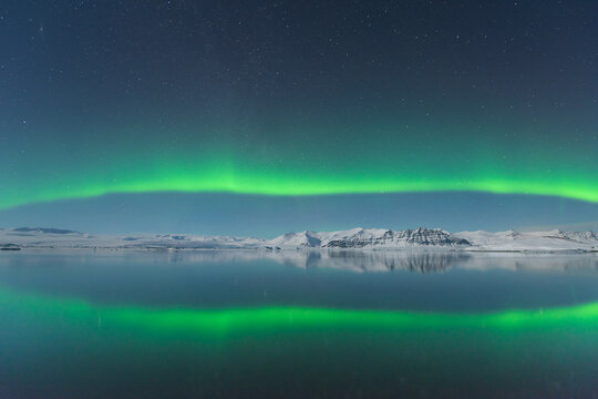 View of the ethereal green aurora borealis dances above the serene, reflective waters, mirroring the celestial display, Jokulsarlon, Sveitarf&eacute;lagio Hornafjorour, Iceland.