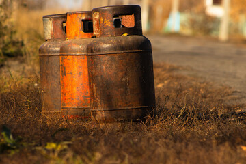 Obraz premium Three Weathered and Rusty Propane Gas Cylinders Standing on Dry Grass in Sunlight