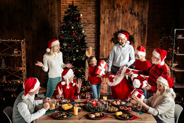Family gathers for Christmas dinner as friends exchange gifts near a lit christmas tree in a cozy...