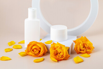 containers for skin care products and yellow rose flowers on a beige background next to geometric shapes