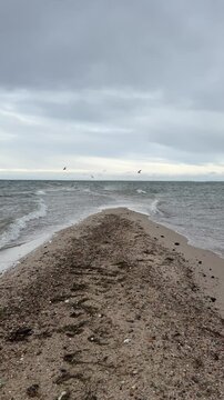 A vertical video capturing the rare natural phenomenon at Rewa, Poland, where waves crash from both sides onto a narrow sandy path stretching into the sea. 