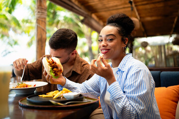 Multiethnic couple enjoying a joyful dining experience by the beach. Great food, perfect summer vibe