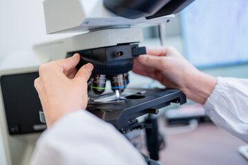 Laboratory technician adjusting microscope for cell analysis in research facility during daytime