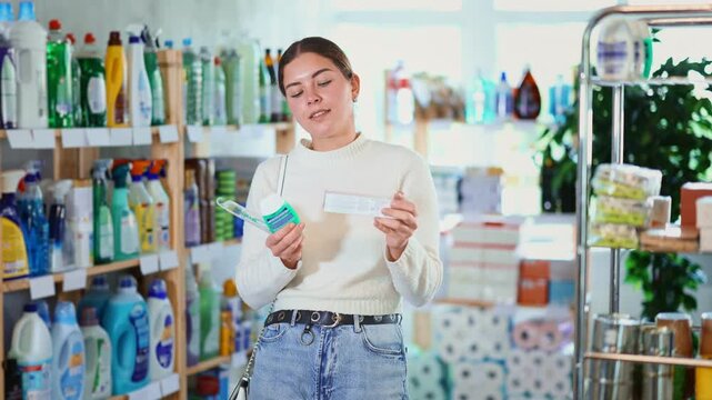 Young woman in the household section of a supermarket chooses products and toothpaste for dental care. High quality 4k footage