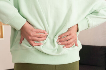 Close-up of person touching lower back in pain, highlighting discomfort and tension. Concept of backache, muscle strain, health care, posture correction and body awareness.
