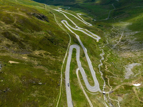 Aerial view of a winding road snaking through the green landscape, cutting through mountains, with cars navigating the sharp turns, Tujetsch, Grisons, Switzerland.