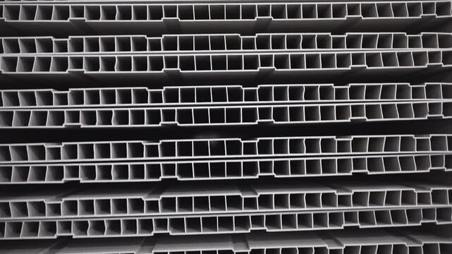 Storehouse contains numerous neatly stacked sheets of PVC profiles. Sheets of PVC profiles designed with complex inner structure to enhance strength and durability