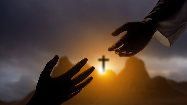 Jesus Christ hand offering a helping hand with Christian cross on the hill with dark dramatic sky background. Concept of Christianity, religious, faith, Jesus, or belief