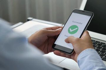 Successful mobile transaction with green checkmark displayed on smartphone screen held by man in office setting