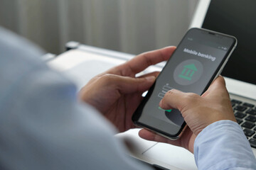 Man using mobile banking app on smartphone while sitting at desk with laptop, concept of digital finance, online transaction, and secure payment technology