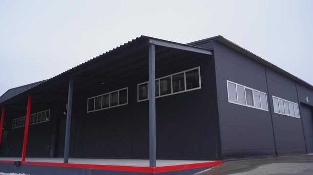 Black industrial storage building with empty freights loading ramp in winter. Modern industrial complex warehouse exterior with red color ornament