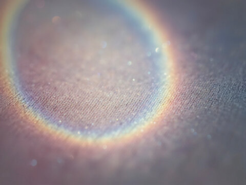 Abstract focus on a circular rainbow light refractor effect with tiny glittering bokeh particles over a subtle, beige textile surface.