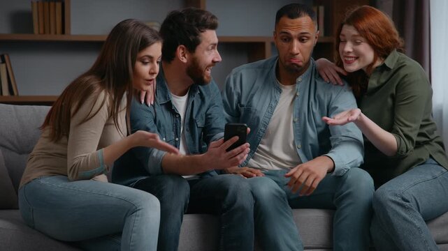 Surprised four multiracial friends at home party looking mobile phone amazed reaction shocked happy diversity men women on couch watching smartphone video wondering excited reading good news achieve