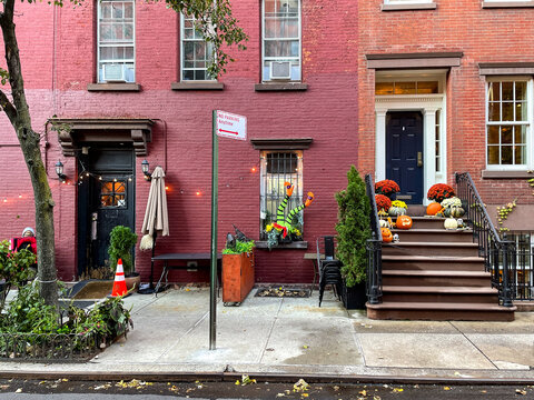 View of brick buildings glow in the soft light of autumn, adorned with pumpkins and potted plants, creating a cozy street scene, New York, New York, United States.