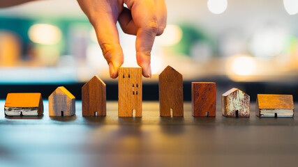 Hand picking a wooden house model among many options, symbolizing real estate investment, property...