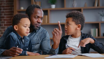 African American family father help son with homework showing one index finger explain irritated pupil talking pointing in notebook problem education dad with two boys sons kids children study trouble