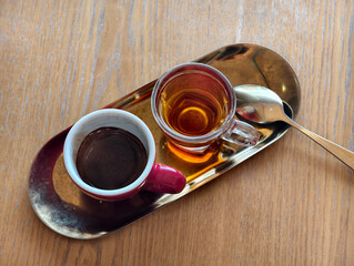 A cup of coffee and a cup of tea served on a golden tray with a spoon on a wooden table. Warm tones and soft natural light create a cozy and inviting caf&eacute; atmosphere.