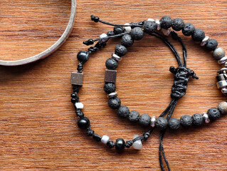 Close-up of handmade black bead bracelets with metal accents on a wooden surface. Minimal and natural jewelry style for product display, craft design, and fashion accessories concepts.