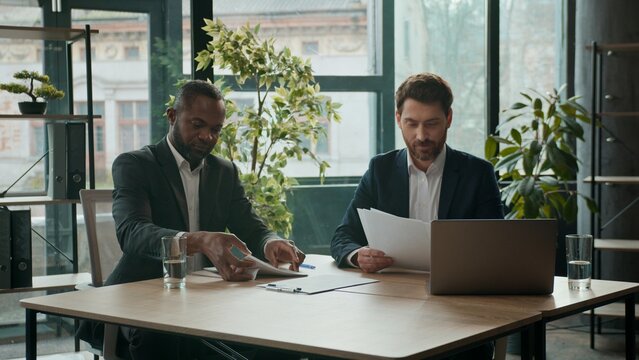 Two diverse smiling business men team businessmen managing documents multiethnic co-workers paperwork cooperate teamwork in office meeting partnership Caucasian African American colleagues with papers
