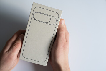 Hands holding a blank smartphone packaging box with a minimalistic design, showcasing the product's potential for branding and customization in a clean, modern setting
