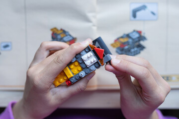 Child's hands assembling colorful building blocks, following instructions from a manual, showcasing creativity and focus in a playful learning environment