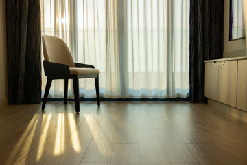 Classic armchair near window with sheer curtain. Sunlight through sheer curtains, casting shadows on laminate floor. The modern room creating serene atmosphere. Copy space for Advertisement or Design.