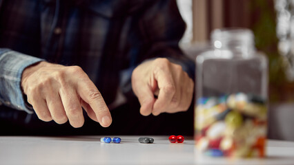 Senior hands choosing colorful pills on white table near medicine bottle. Concept of pharmacy advertising, e-commerce catalog visuals, and medical education materials.