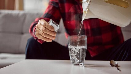 Senior man pouring hot water into glass while preparing powdered medicine drink. Concept of pharmacy packaging design, wellness advertising, and health instruction.