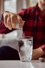 Older man adding medicine powder into glass of water during home treatment. Concept of wellness education, pharmacy advertising, and medical instruction.