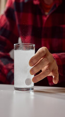 Elderly hand touching glass with dissolving effervescent tablet in water. Concept of pharmacy advertising, dosage instruction, and preventive healthcare.