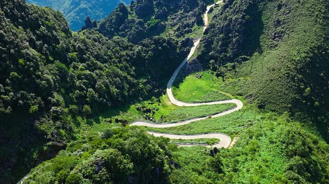 Aerial shot of a winding mountain road with sharp hairpin turns snaking through a spectacular lush green valley in Guizhou, China.