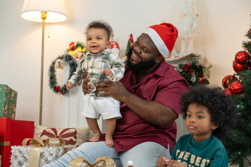 Happy African American dad with two son children celebrating Christmas. Black father and kids opening Christmas gifts.