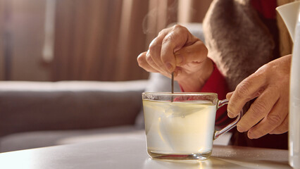 Elderly hand stirring yellow dissolved medicine drink in transparent mug. Concept of pharmacy...