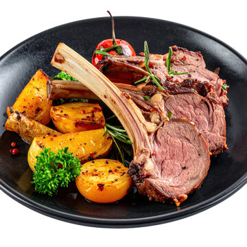 Grilled lechazo asado roast lamb chops with roasted potatoes rosemary and cherry tomato on black plate isolated white background