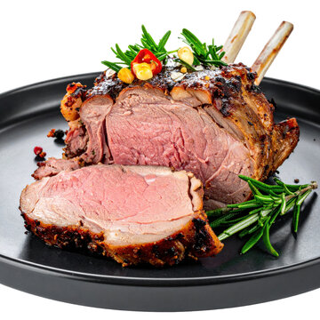 Roasted rack of lechazo asado roast lamb with fresh rosemary and garnishes on black plate isolated white background