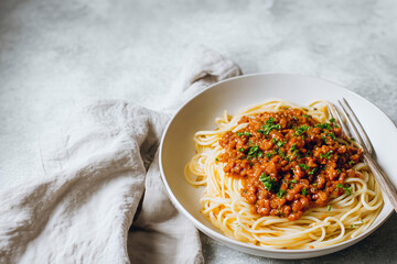 Delicious spaghetti bolognese with meat sauce and parsley served on a white plate on a light background