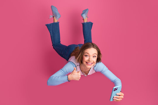 Charming young woman taking a selfie with a smartphone on a vibrant pink background, exuding happiness and charm