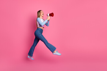 Cheerful young woman in casual outfit with megaphone against vibrant pink background expressing...