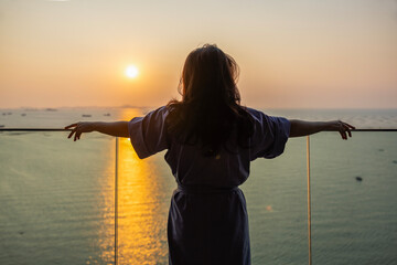 Businesswoman standing at balcony looking Beautiful view sunrise over sea, fresh air, getting ready for new day, Relax, Wake up, Thinking. Woman enjoying her holiday in luxury hotel or apartment. 