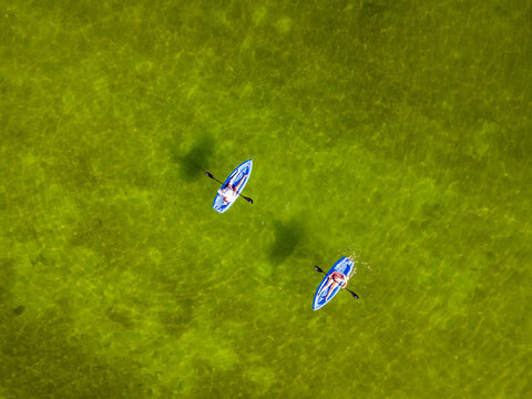 Aerial view of two vivid blue kayaks glide across the shimmering, translucent green waters, creating a striking contrast of color and texture., Progreso, Yucatan, Mexico.