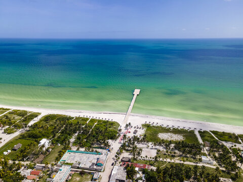 Aerial view of a pier stretching out into the turquoise waters, the coastline fringed with white sand and verdant trees, Progreso, Yucatan, Mexico.