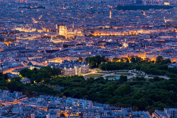 Aerial view of Paris at dusk with illuminated Notre Dame Cathedral on Ile de la Cite, Luxembourg Gardens, and the Latin Quarter. Scenic twilight cityscape of the capital of France