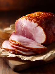 close-up of sliced roasted ham with glossy caramelized surface and pink interior arranged on parchment paper atop wooden cutting board in rustic warm setting