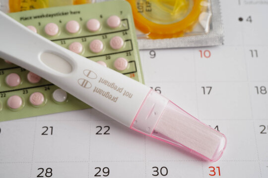 Pregnancy test with birth control pills and condom for female on calendar, ovulation day.