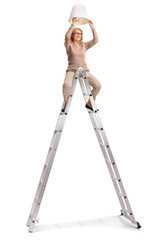 Woman sitting on a tall ladder and changing a light bulb