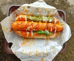 Delicious hotdog with sauce and lettuce on paper wrap
