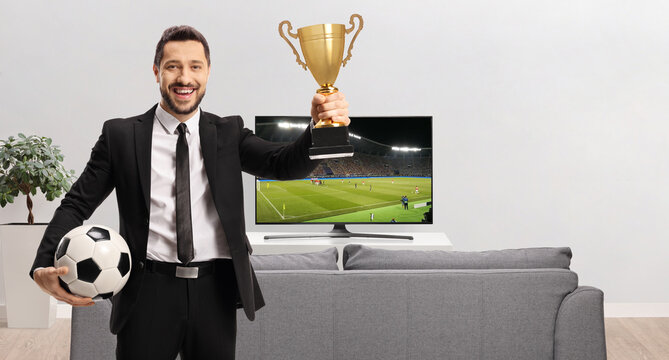 Man at home holding a trophy cup and football - Powered by Adobe