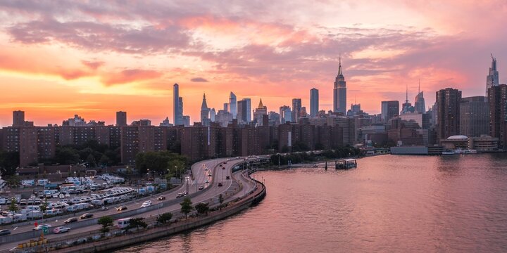 Aerial view of the city's skyline glows with the setting sun, casting a warm hue over the East River and the iconic Empire State Building, New York, New York, United States.