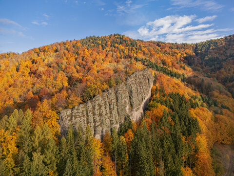 Aerial view of a dramatic rock face standing out amidst a sea of vibrant autumn foliage on Janosikova skala, Hrochot, Banska Bystrica Region, Slovakia.