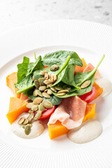 modern, gourmet salad featuring spinach, orange segments, and smoked seafood, garnished with pumpkin seeds on a minimalist white plate against a gray speckled background.